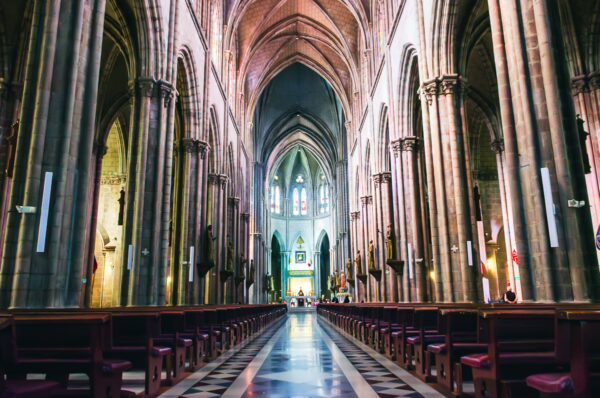 Stunning interior of Basilica del Voto Nacional features tall arches, intricate details, and rows of wooden pews in Quito, Ecuador.
