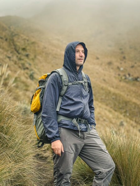 Hiker in a blue jacket stands on a misty trail near Imbabura Volcano, surrounded by tall grasses and rugged terrain in Ecuador.
