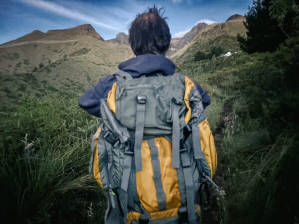 Hiker with a backpack gazes towards the scenic Imbabura Volcano in Ecuador, surrounded by lush greenery and rugged terrain.