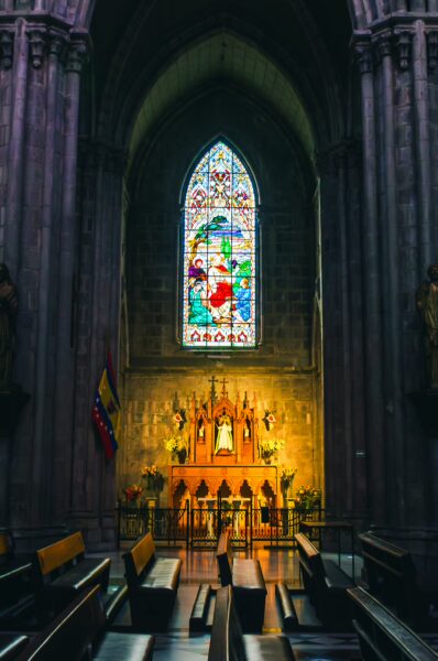 Stained glass illuminates the altar inside Basilica del Voto Nacional, showcasing colorful details and wooden pews in Quito, Ecuador.