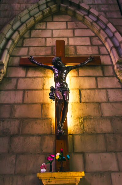 Crucifix on a stone wall illuminated by soft light, with flowers at the base in Basilica del Voto Nacional, Quito, Ecuador.