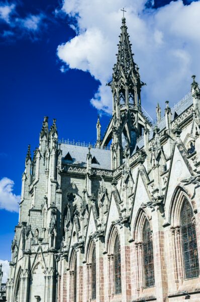 Stunning Gothic architecture of Basilica del Voto Nacional rises against a bright blue sky in Quito, Ecuador, showcasing detailed spires.