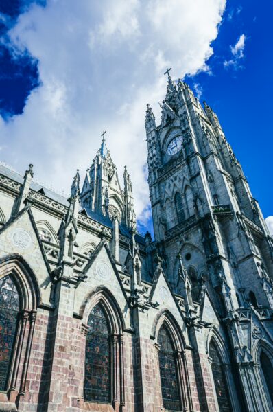 Basilica del Voto Nacional stands tall in Quito, Ecuador, showcasing intricate stonework and dramatic clouds against a bright blue sky.