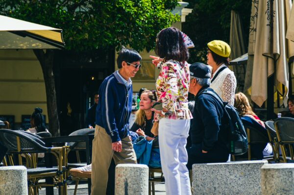 People engage in conversation at Plaza Ramales, surrounded by outdoor seating, greenery, and vibrant umbrellas in Madrid, Spain.