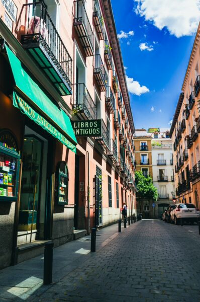 Charming street in Madrid, Spain, showcasing colorful buildings, antique bookshop signage, and clear blue skies.