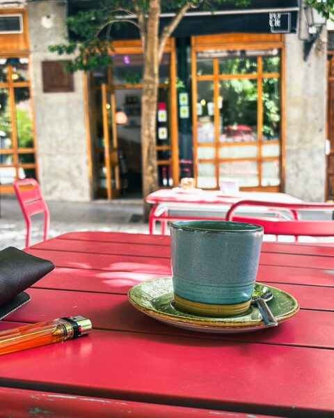 Specialty coffee in a colorful cup on a vibrant red table, with a blurred view of Madrid's charming street scene.