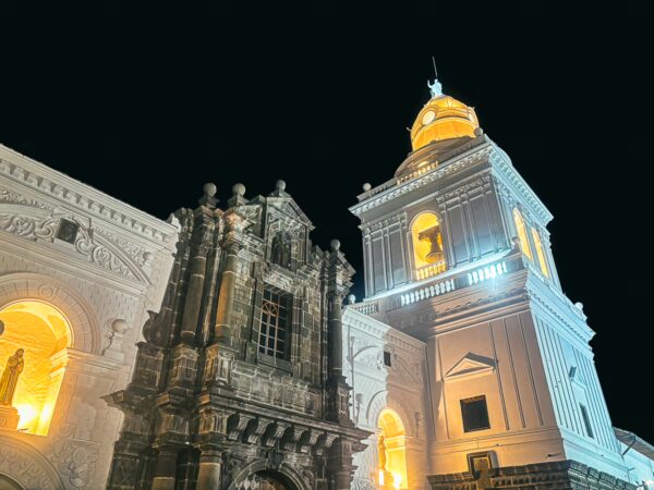 San Agustín Church illuminated at night, showcasing its intricate facade and prominent clock tower in Quito, Ecuador.