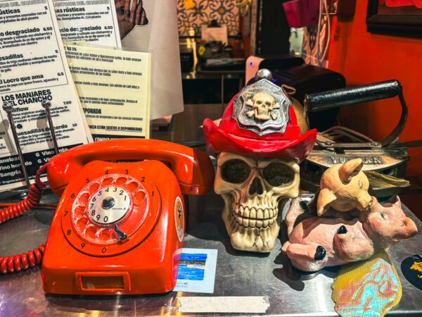 Colorful decor at Andes Brew Pub in Quito features an orange rotary phone, a skull wearing a hat, and quirky animal figurines.