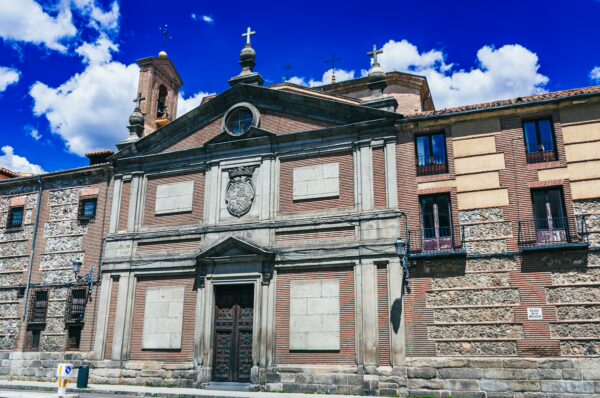 Monasterio de las Descalzas Reales features intricate stonework and a grand facade against a bright blue sky in Madrid, Spain.