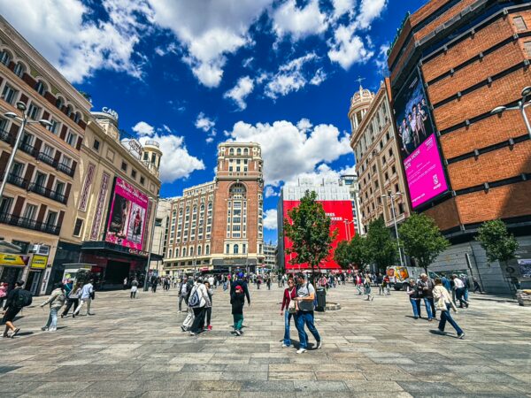 Bustling Plaza del Callao showcases vibrant architecture, lively crowds, and dramatic clouds in Madrid, Spain.