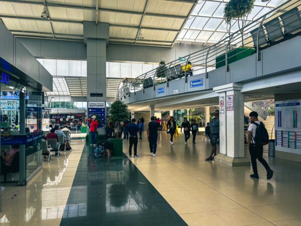 Modern interior of Quitumbe Terminal Terrestre in Quito, Ecuador, showcasing spacious layout, travelers, and greenery.