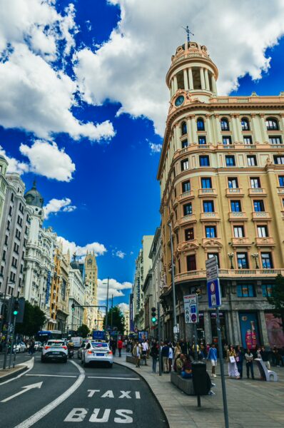 Bustling street scene at Plaza del Callao in Madrid, featuring historic architecture, blue skies, and vibrant city life.
