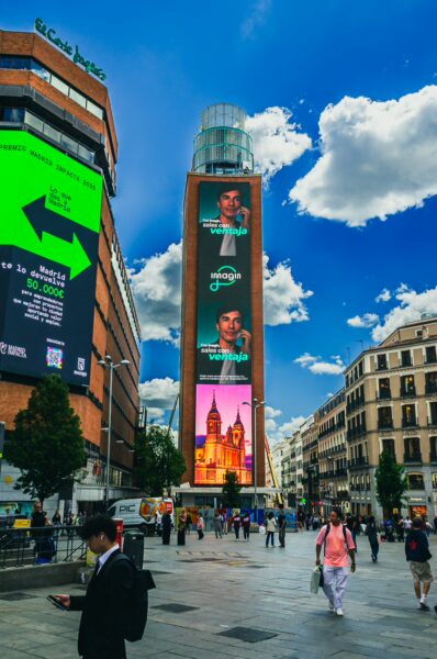 Plaza del Callao features a vibrant tower adorned with colorful advertisements against a bright blue sky in Madrid, Spain.