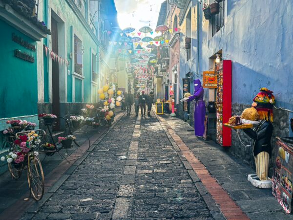 Vibrant La Ronda features cobblestone streets, colorful umbrellas overhead, flowers, and street performers in Quito, Ecuador.