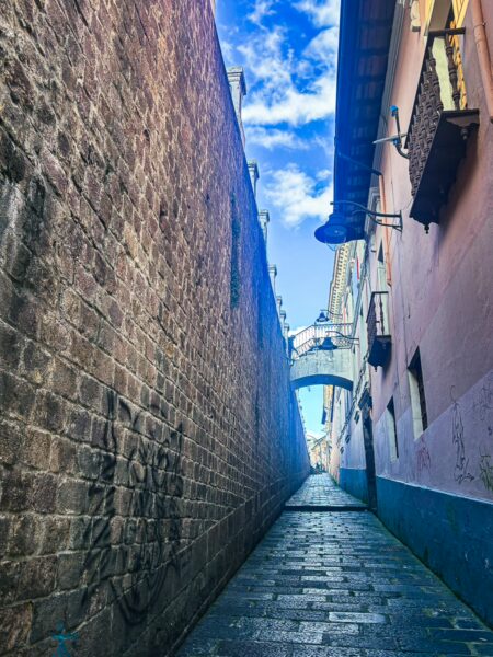Narrow stone alley with vivid blue sky, leading towards La Ronda and Juan de Dios Morales Street in Quito, Ecuador.