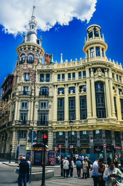 Historic architecture featuring ornate details and a vibrant sky in Madrid, Spain, with pedestrians gathered below.