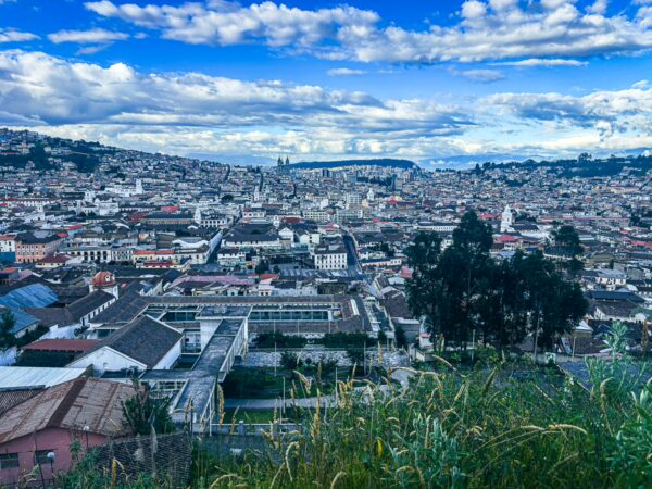 Vibrant cityscape of Quito, Ecuador, showcases historic buildings, lush greenery, and a backdrop of dramatic cloud formations.