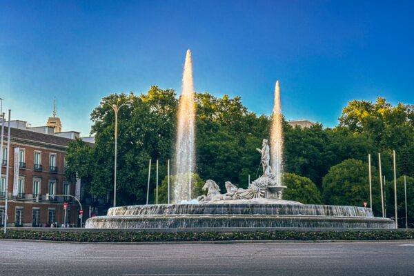 Neptune Fountain in Madrid, Spain, features elegant sculptures and jetting water, surrounded by lush greenery against a clear sky.