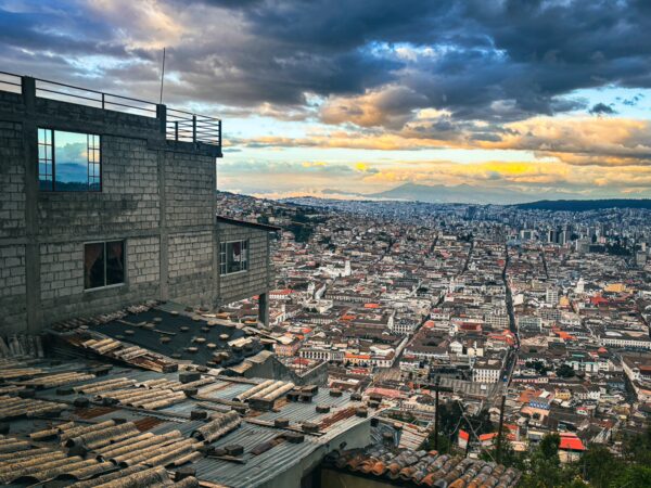Vibrant cityscape of Quito, Ecuador, showcasing rooftops and the Andes mountains under a cloudy sky at sunset.
