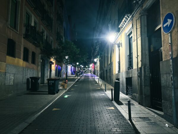 Quiet nighttime street in Madrid, Spain, featuring warm streetlights illuminating the cobblestones and colorful guides along the way.