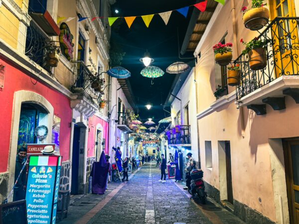 Colorful buildings line Juan de Dios Morales Street in La Ronda, Quito, adorned with festive lights and hanging plants.