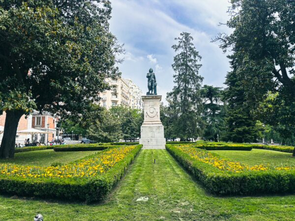 Statue surrounded by vibrant flower beds in a well-maintained garden in Madrid, Spain, capturing a peaceful outdoor scene.