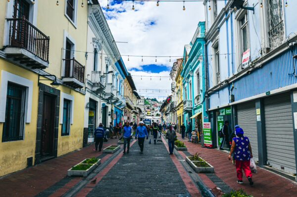 Bustling street in Quito, Ecuador, featuring colorful colonial buildings, pedestrians, and decorative string lights.