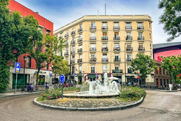 Elegant fountain surrounded by lush greenery and colorful buildings in a vibrant Madrid square.