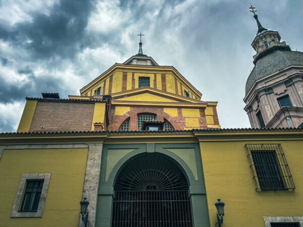 Historic architecture in vibrant colors highlights Madrid, Spain, beneath a dramatic sky, showcasing ornate rooftops and detailed facades.