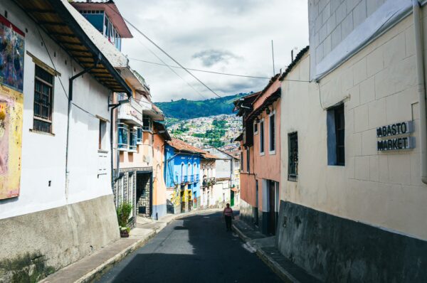 Colorful buildings lining Vicente León street with a view of distant hills in Quito, Ecuador, under a cloudy sky.