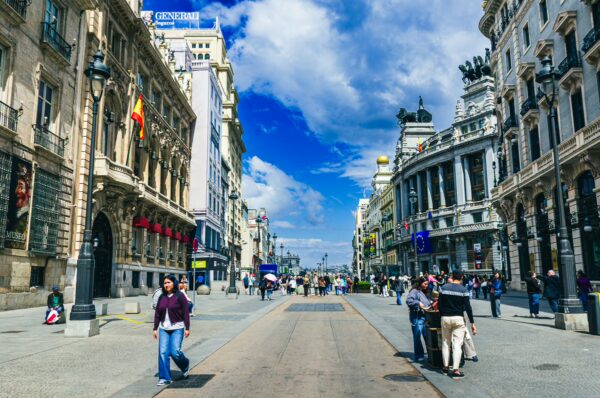 Bustling street scene in Madrid, Spain, featuring historic buildings, vibrant blue skies, and people enjoying the lively atmosphere.