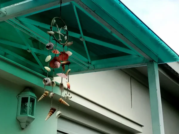 Colorful seashell wind chime hanging from a teal roof overhang against a light-colored building in Chalkis.