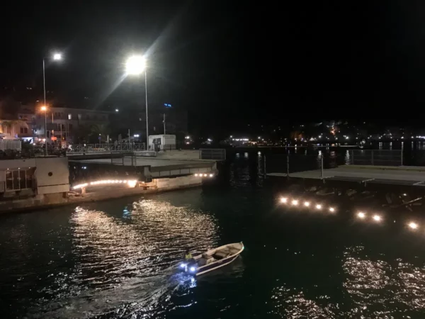Small boat gliding through calm waters at night, with illuminated harbor features and reflections in Chalkis.