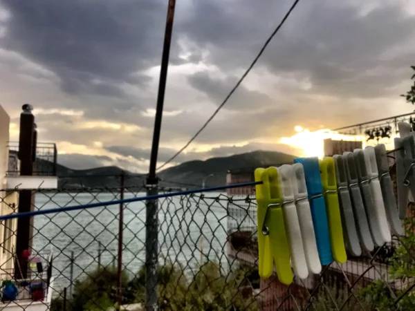 Clothespins in bright colors hang on a line, with a serene view of Chalkis' coastline and dramatic skies at sunset.