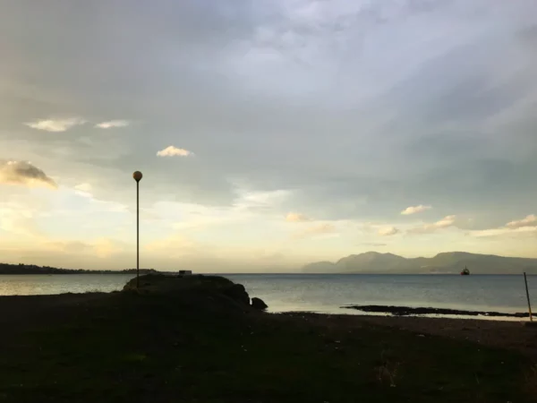 Tranquil sunset over the water at Chalkis, featuring a solitary lamp post and distant mountains on the horizon.