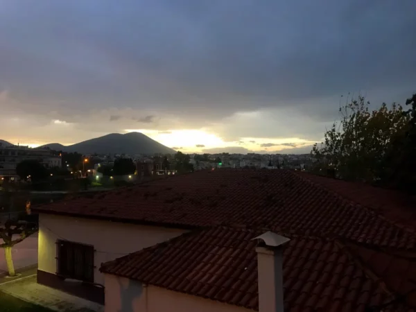 Sunset over rooftops with terracotta tiles, casting a warm glow against the darkening sky in Chalkis.