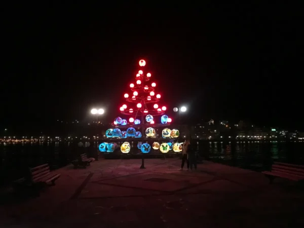 Colorful Christmas tree lights illuminate the waterfront in Chalkis at night, creating a festive atmosphere by the water.