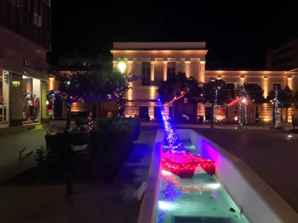 Illuminated fountains adorned with vibrant blue and red lights create a festive atmosphere at night in Chalkis.