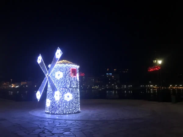 Colorful illuminated windmill with decorative lights by the waterfront, creating a festive atmosphere in Chalkis at night.