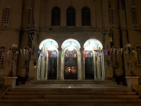 Elegant entrance of a historic building with illuminated arches and colorful flags, set against a night sky in Chalkis.