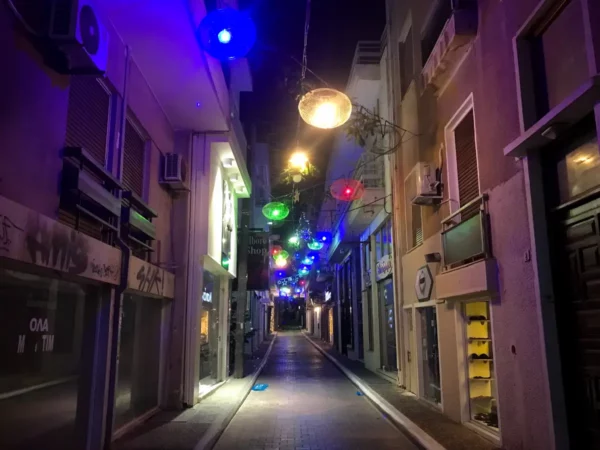 Colorful lights illuminate a narrow street in Chalkis, showcasing vibrant shop fronts and a lively nighttime atmosphere.