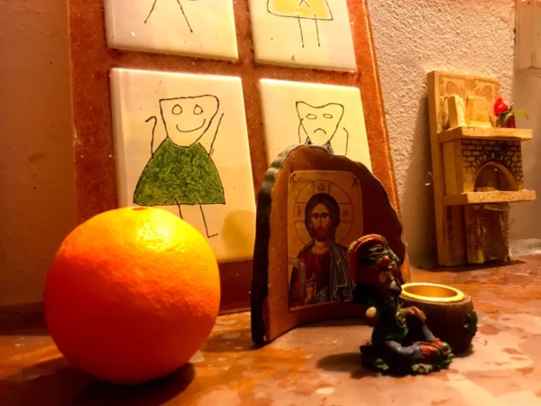 Vibrant orange fruit sits beside an icon of a saint and a small figurine on a rustic surface in Chalkis.