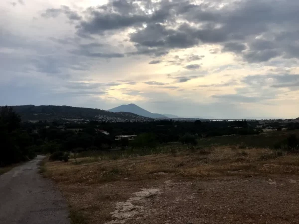 Sunset view over Chalkis, highlighting rolling hills, a winding path, and a dramatic sky filled with clouds.