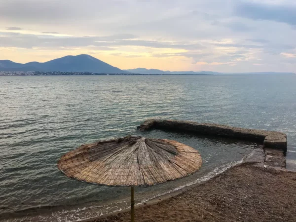 St straw umbrella on a sandy beach with calm waters and mountains in the distance at sunset in Chalkis.