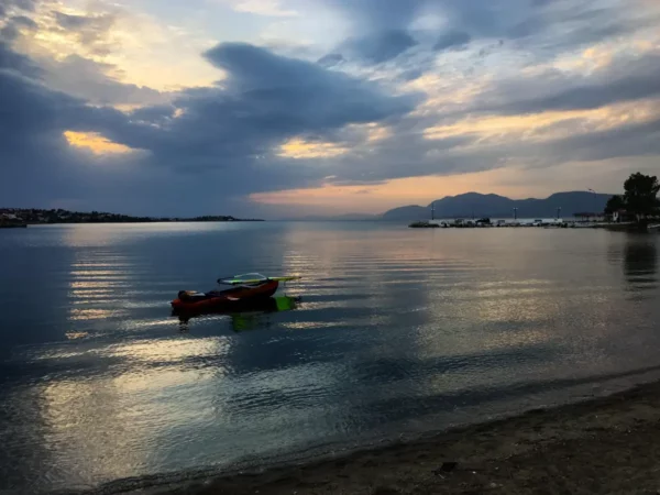 Calm waters at sunset reflect a colorful sky, with a lone kayak anchored near the shore in Chalkis.