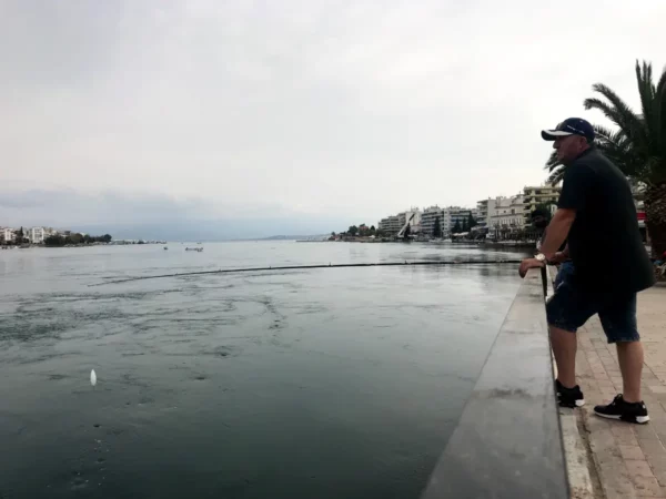 Man fishing along the waterfront in Chalkis, with calm waters and picturesque buildings lining the shore in the background.