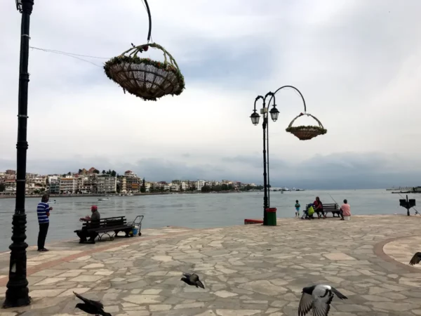 Charming waterfront scene in Chalkis with decorative hanging baskets, benches, and people enjoying the serene view by the water.