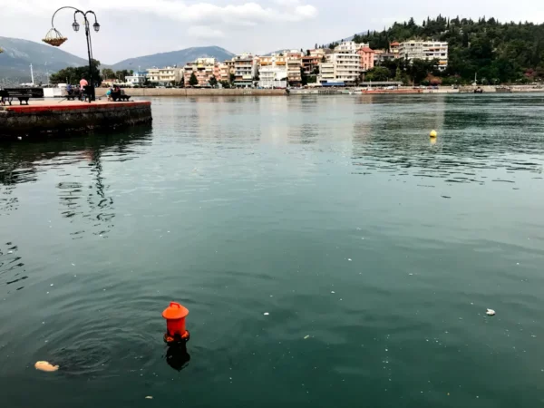 Vibrant orange buoy floats in the calm water, with Chalkis' charming waterfront buildings visible in the background.