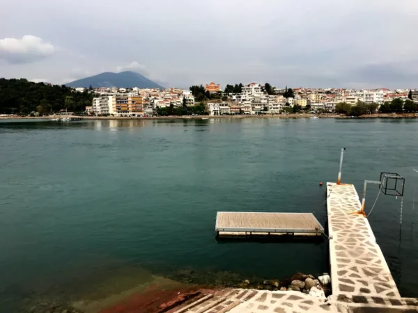 Chalkis waterfront with calm turquoise waters, white buildings lining the shore, and a distant mountain backdrop.