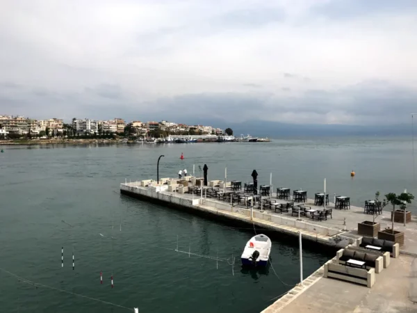 Serene waterfront view in Chalkis features a dock with a boat, empty tables, and a calm sea under a cloudy sky.